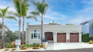 A modern two-story house with a garage, palm trees, and a well-maintained front yard.