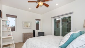 A bedroom with a bed, a ceiling fan, a bookshelf, a dresser, and a window with blinds.