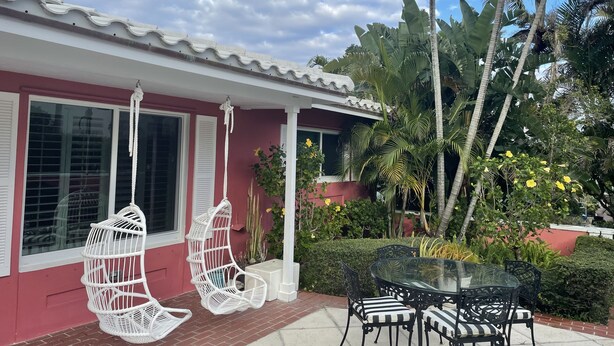 A house with a red exterior, white shutters, and a porch with white wicker chairs and a glass table with black chairs. - Oceanfront Beach Cottage with Private beach access in beautiful Juno Beach. (Juno Beach)