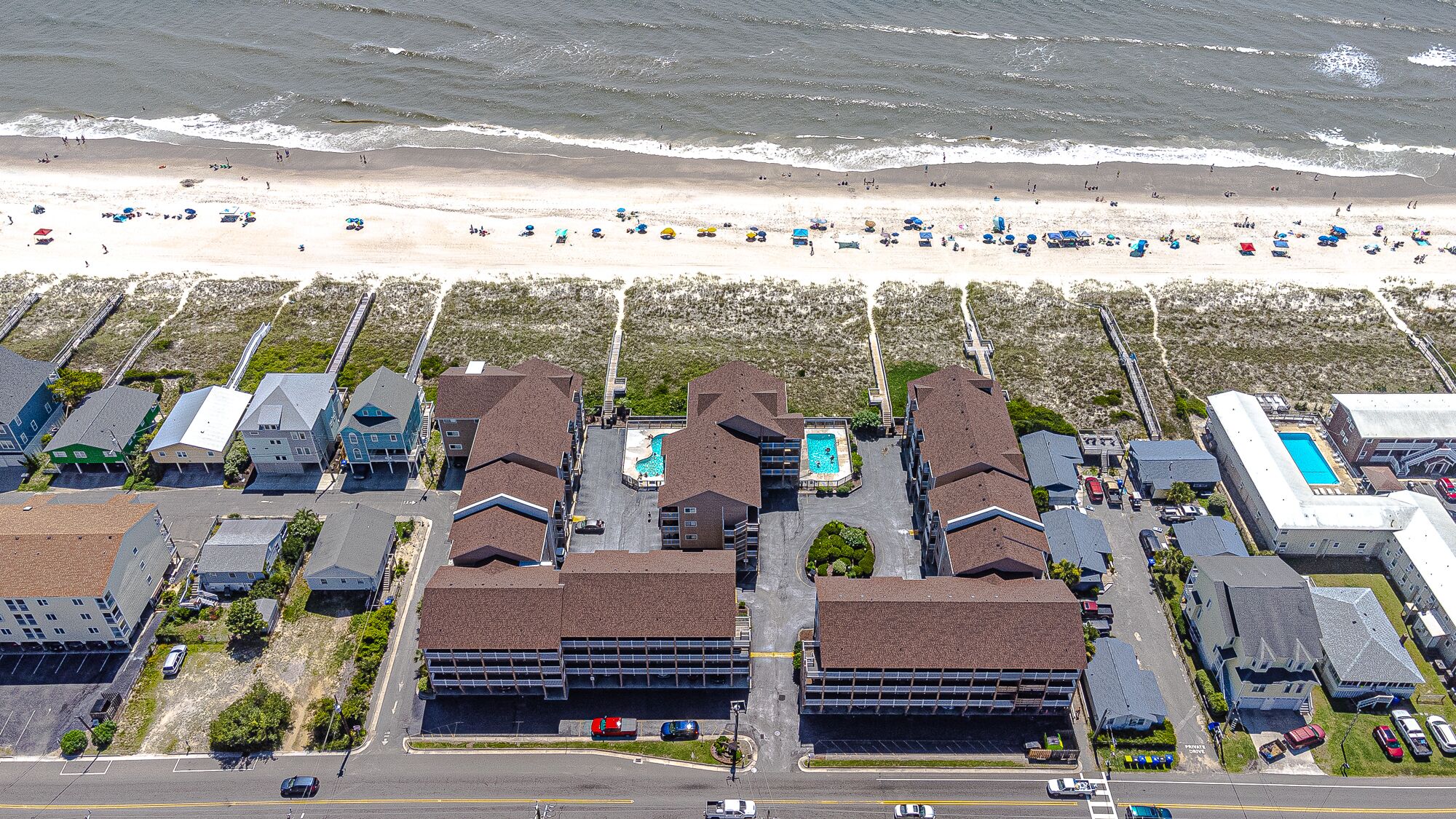 Un hôtel situé sur la côte, composé de plusieurs bâtiments, doté d’un parking et donnant sur une plage équipée de parasols.