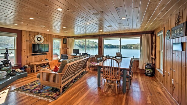 A cabin with a wooden interior, a large window overlooking a lake, a dining area, and a cozy seating area. - BBQ Ready: Lakeside Milford Home w/ Paddleboat (Milford)