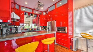 Una cocina moderna con armarios rojos, electrodomésticos de acero inoxidable y una isla central con taburetes amarillos.