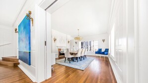 Amplia habitación luminosa con pisos de madera, un comedor con candelabro y un cuadro grande en la pared.