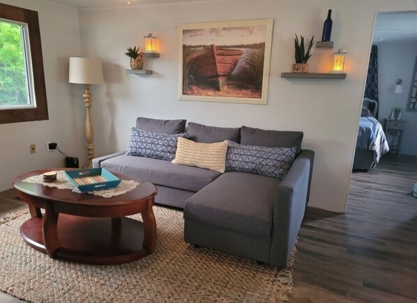 A living room with a sofa, a round wooden coffee table, a lamp, and wall-mounted shelves with decorative items.