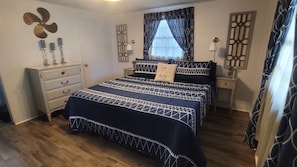 A bedroom with a bed, dresser, nightstands, and a window with curtains.