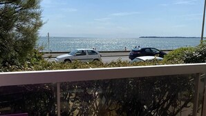A balcony with a purple table, overlooking a coastal road with parked cars and a view of the sea.