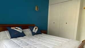 A neatly made bed with white bedding and two pillows, a wooden headboard, and a woven hanging light fixture.