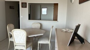 A dining area with a marble table, two upholstered chairs, a wooden desk with a computer, and a large mirror on the wall.
