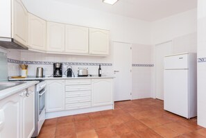 Una cocina con armarios blancos, cafetera, tostadora y refrigerador.
