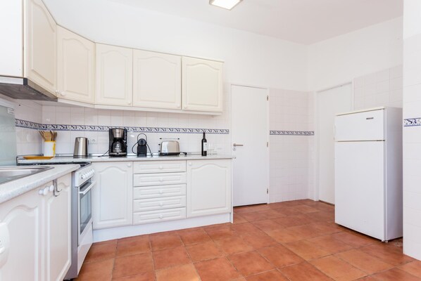 Una cocina con armarios blancos, cafetera, tostadora y refrigerador.