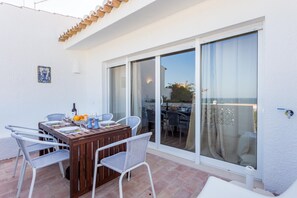 A patio with a wooden table set for dining, surrounded by wicker chairs, and a sliding glass door leading to an outdoor area.