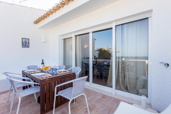 A patio with a wooden table set for dining, surrounded by wicker chairs, and a sliding glass door leading to an outdoor area.