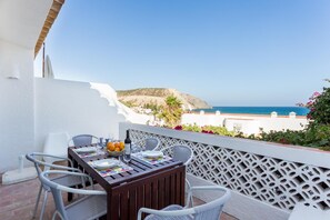 Ein Balkon mit Tisch für zwei Personen, mit Blick auf die Küste und ein Berg in der Ferne.