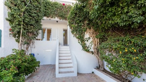 Un edificio blanco con una escalera que lleva a una puerta, rodeado de follaje y plantas.
