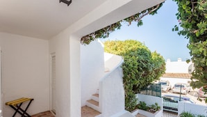 Habitación de paredes blancas con un pequeño banco de madera y una escalera que lleva a un jardín con plantas y vistas a coches aparcados.