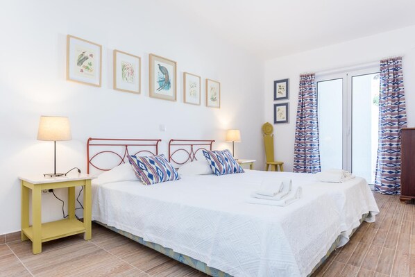 Una habitación de hotel con cama, mesitas de noche, una lámpara, una silla y una ventana con cortinas.