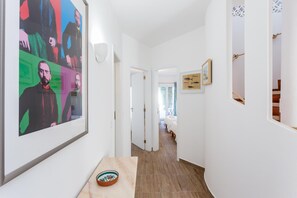 A hallway with a large abstract painting, a bowl on a table, and a framed picture on the wall.