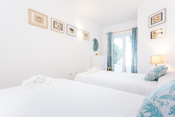 A hotel room with two beds, a dresser, a mirror, and framed pictures on the wall.