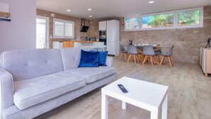 En moderne stue med en grå sofa, et hvidt sofabord og et spiseområde med grå stole og et træbord.