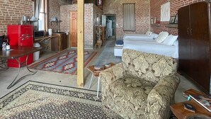 A room with a brick wall, a wooden ceiling beam, a bed with patterned bedding, a red appliance, and a patterned rug. - Unique 1870's building with outdoor space to relax (McDade)