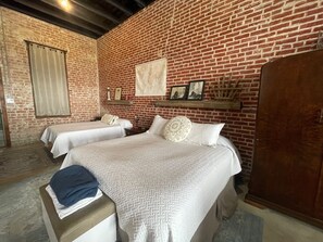 A room with two beds, a wooden wardrobe, and a brick wall. - Unique 1870's building with outdoor space to relax (McDade)