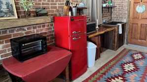 A compact kitchen with a red refrigerator, a black toaster oven, and a wooden bench. - Unique 1870's building with outdoor space to relax (McDade)