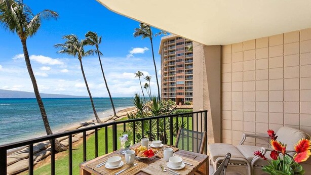 Un balcon avec une table dressée pour le petit-déjeuner, donnant sur une plage bordée de palmiers et offrant une vue sur l’océan.