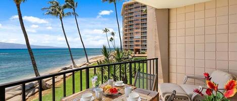 Un balcon avec une table dressée pour le petit-déjeuner, donnant sur une plage bordée de palmiers et offrant une vue sur l’océan.