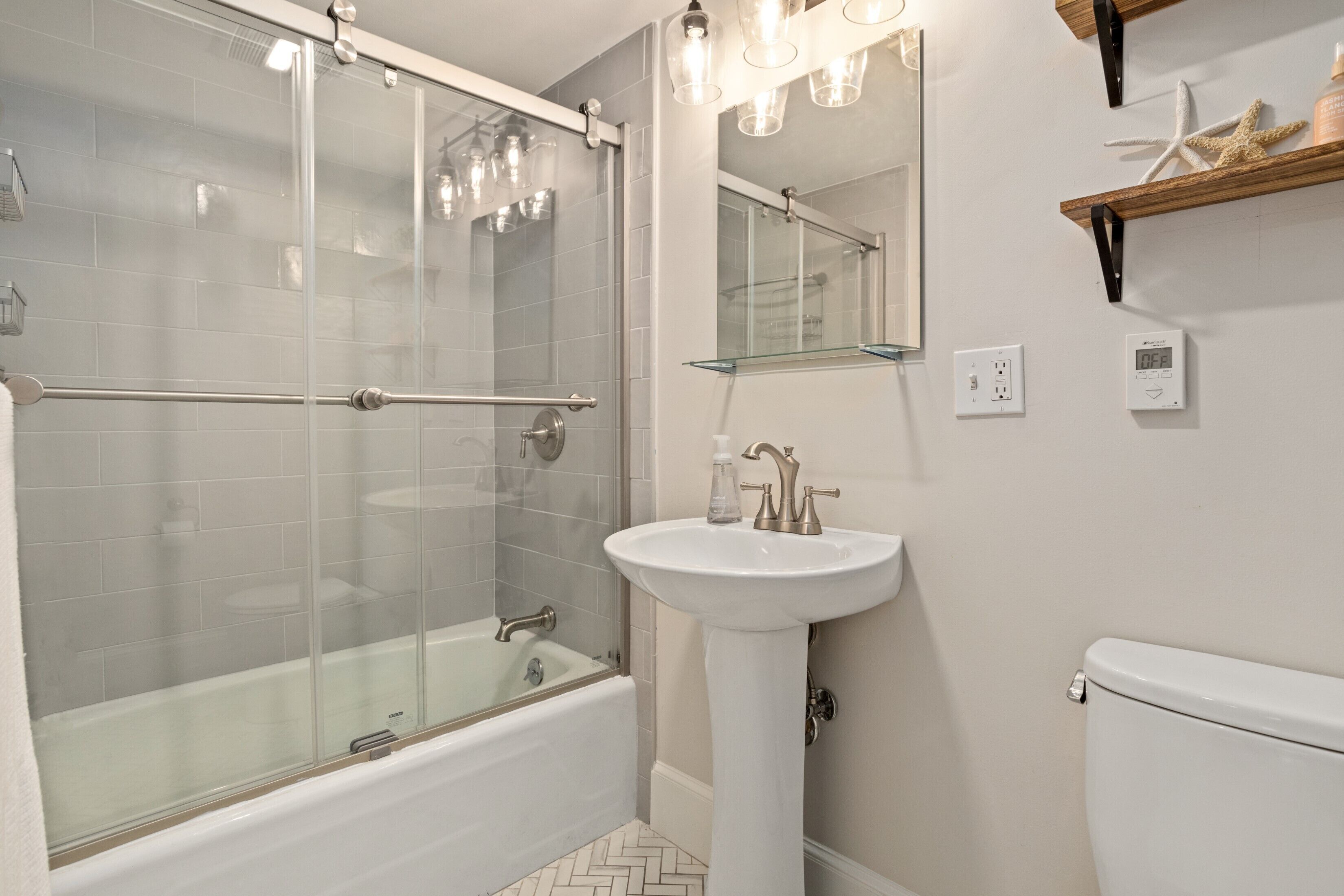 A modern bathroom with a glass-enclosed shower, a freestanding bathtub, a pedestal sink, and a toilet.