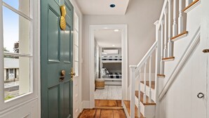 A hallway with a green door, wooden flooring, and a staircase with white railings.