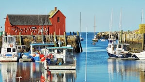 A harbor with boats docked, a red building, and a stone wall.