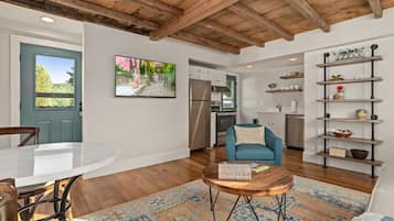 Un salon moderne avec un plafond en bois, une table à manger, un fauteuil bleu, une table basse et une cuisine en arrière-plan.