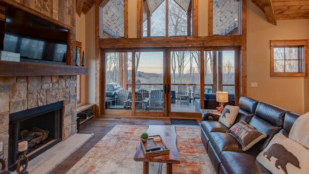 A spacious living room with a stone fireplace, leather sofa, and large sliding glass doors leading to an outdoor deck. - Happy Trails - Pet friendly Eagles Nest with view, hot tub, fire pit (Banner Elk)
