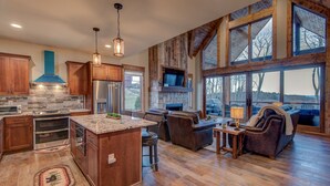 A spacious kitchen with a large island, wooden cabinets, and a stone backsplash. There is a cozy seating area with a leather sofa and a massage chair. - Happy Trails - Pet friendly Eagles Nest with view, hot tub, fire pit (Banner Elk)