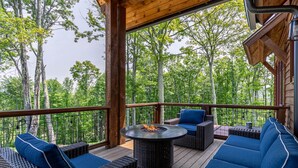 A covered outdoor deck with wicker furniture and a fire pit. - Happy Trails - Pet friendly Eagles Nest with view, hot tub, fire pit (Banner Elk)
