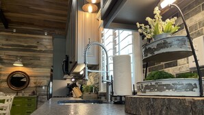 A kitchen with a granite countertop, stainless steel appliances, and a hanging pot rack with white flowers. - Elegant Country Cottage (Crawford)