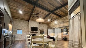 A spacious kitchen with a dining area, wooden ceiling beams, a stone wall, and a large window. - Elegant Country Cottage (Crawford)