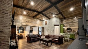 A spacious living area with a high ceiling, wooden beams, and a large window. There is a brown leather sofa and a coffee table. - Elegant Country Cottage (Crawford)