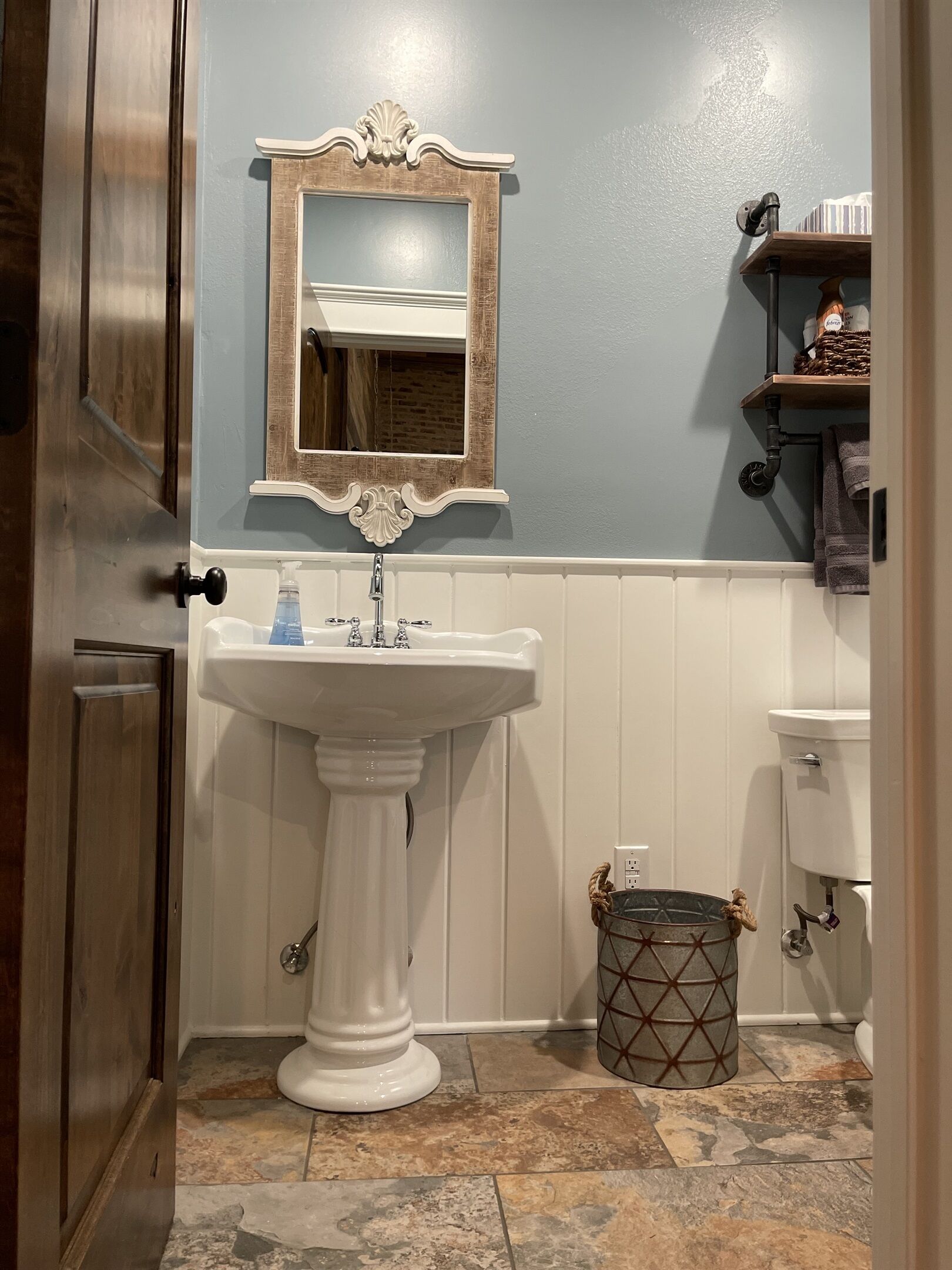 A bathroom with a pedestal sink, a wall-mounted mirror, a toilet, and a trash can.