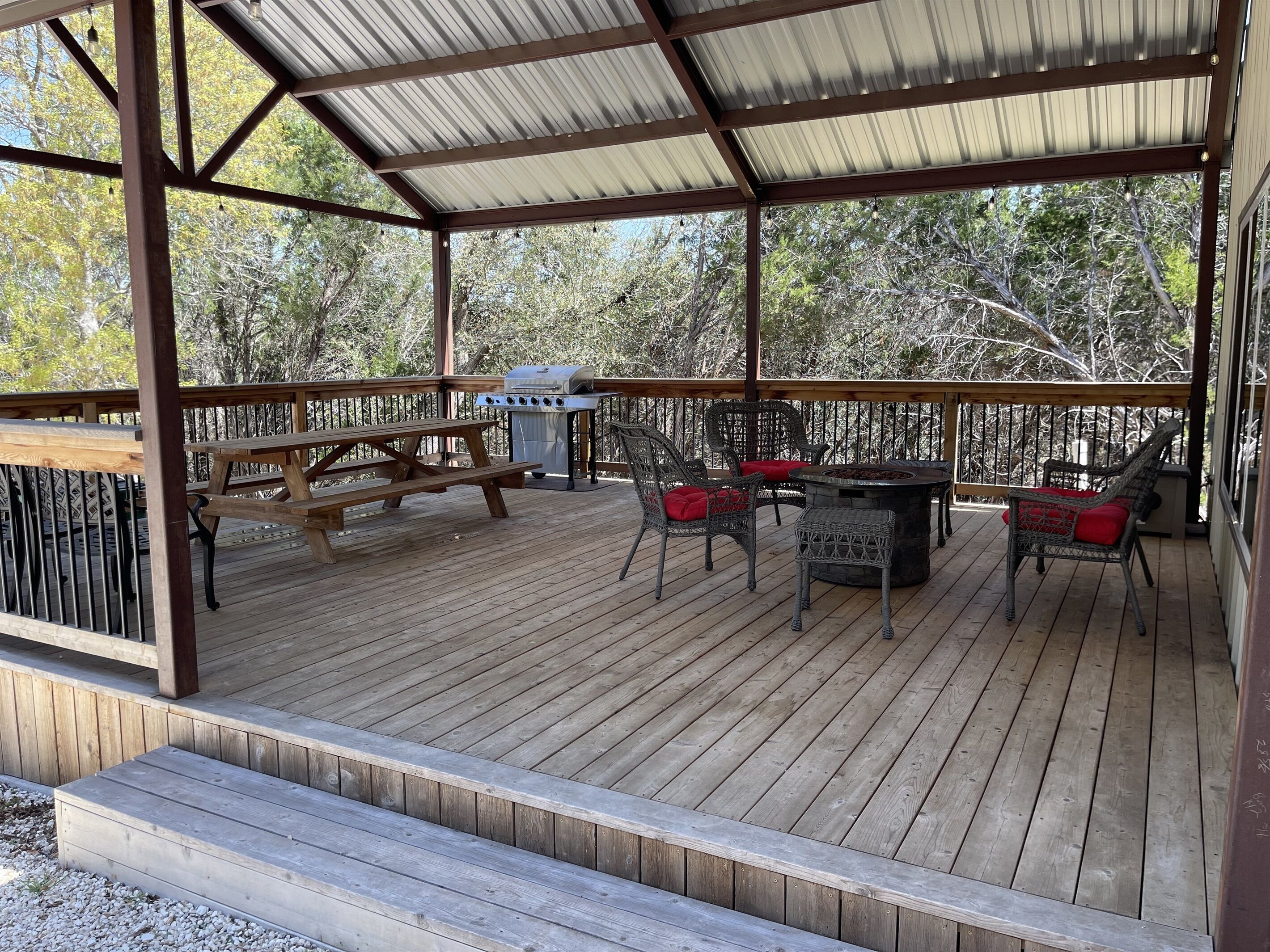 A covered outdoor deck with picnic tables and wicker chairs, a grill, and a fire pit.