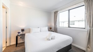 Ett hotellrum med en stor säng, ett nattduksbord med en lampa och ett fönster med gardiner.