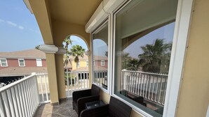 A balcony with two wicker chairs, a tiled floor, and a view of neighboring houses and palm trees. - Town home in the Marina  38 HT (Laguna Vista)