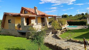 A two-story house with a stone facade, a red-tiled roof, and a stone staircase leading to a wooden deck. - Melograno by Interhome (Lago di Vico)