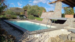 A swimming pool with lounge chairs and an umbrella, surrounded by a stone wall and greenery. - Melograno by Interhome (Lago di Vico)
