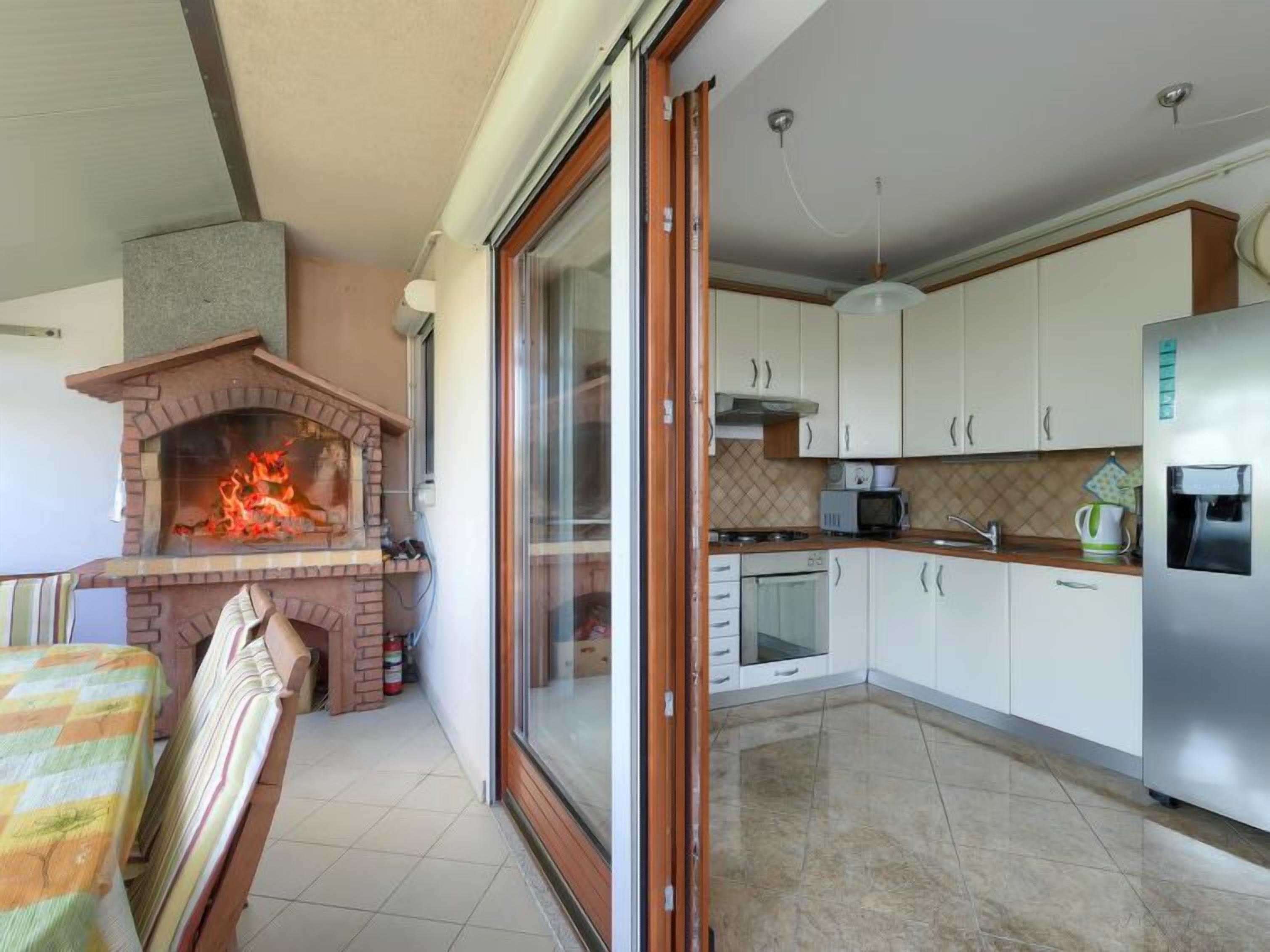 A kitchen with a brick fireplace, white cabinets, a stainless steel refrigerator, and a dining area with a striped tablecloth.