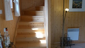 Una escalera de madera que sube a un piso superior, una lámpara de pie y un radiador fijado a la pared.