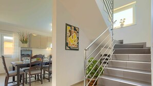 A modern kitchen with a dining area, a staircase with a metal railing, and a potted plant on the landing.