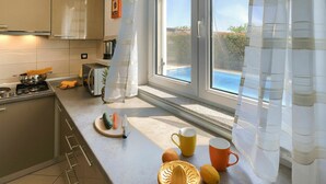 A modern kitchen with a stove, a microwave, and a window overlooking a swimming pool.
