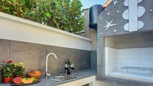 An outdoor kitchen with a sink, a cutting board, and a bowl of fruit.