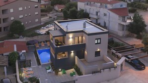 A modern two-story house with a swimming pool, a covered patio, and a car parked in the driveway.